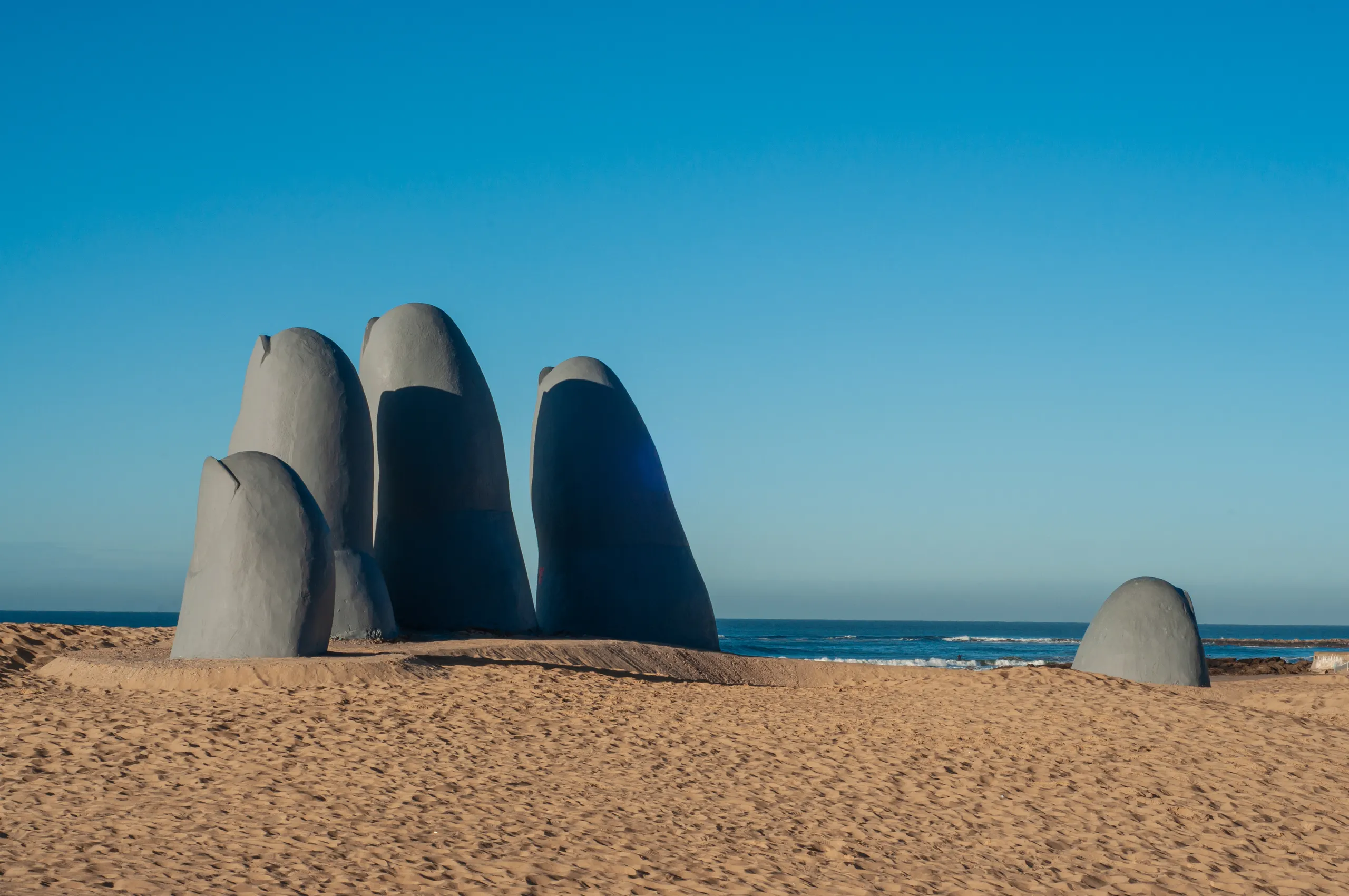 La escultura La Mano saliendo de la arena en la playa Brava